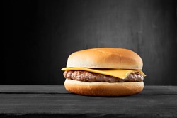 Plain beef burger with cheese on wooden table isolated on black background.