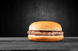Plain beef burger on wooden table isolated on black background.