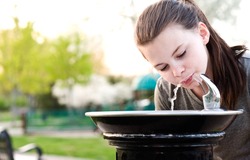 An image of a young girl drinking from a water fountain