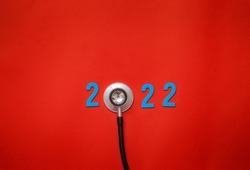 Wooden colorful on text 2022 banner for health care and medical concept. black stethoscope,on table red background.