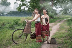 Beautiful girls wearing Thai traditional dress in the countryside takes her bicycle back from the rice fields and random catch fish on bike. One holding a vintage tiffin container.Portrait smile