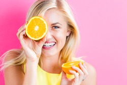 Happy young woman holding oranges halves on a pink background