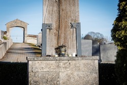 A lantern and three grave lights on a stone pedestal with gravestones in the background and view of the cemetery gate in front of a blue sky in Wessobrunn, Bavaria