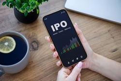 female hands hold phone with IPO stocks purchase app on screen at table in office 