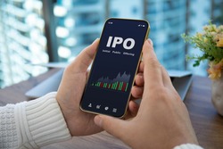 male hands hold phone with IPO stocks purchase app on screen against background of office 