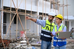 Young attractive construction man and woman in vest with helmet working with laptop on building construction site. Home building project. Engineer foreman discusses with a coworker at workplace