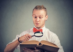 Portrait of a young man reading an interesting book with magnifying glass 