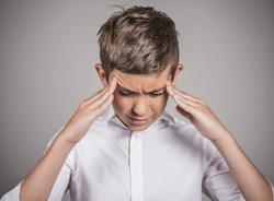 Closeup portrait stressed sad teenager boy hands on temples, head spinning around, overwhelmed at school in life isolated grey background. Negative human facial expression emotion feeling, perception