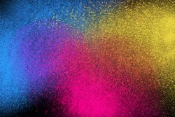 Freeze motion of colorful powder exploding isolated on dark black background. Abstract explosion design of yellow blue magenta, purple, violet dust. Particles cloud wallpaper.