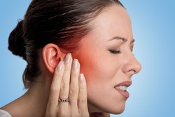 Tinnitus. Closeup up side profile sick female having ear pain touching her painful head isolated on blue background 