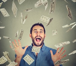Happy young man going crazy screaming super excited. Portrait ecstatic guy celebrates success under money rain falling down dollar bills banknotes isolated gray background. Financial freedom concept