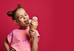 Pretty baby girl kid eating licking big ice cream in waffles cone with raspberry happy laughing on red background