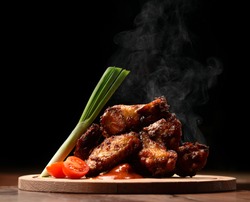 Hot and spicy bbq chicken wings with dip and hot sauce on wooden plate with steam smoke and vegetables