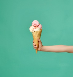 Baby kid hand holding big ice-cream in waffles cone on blue mint background