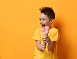 Baby boy kid eating strawberry ice-cream in waffles cone happy screaming laughing on yellow background with free text copy space