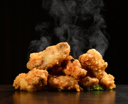 Hot and spicy bbq chicken wings with with green salad leaf and steam smoke on black background