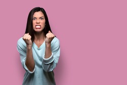Woman with extreme rage, clinched fists and jaw, angry, emotional, and furious, isolated on pink background, copy space