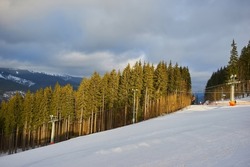Ski resort in beautiful sunset light. View from the top: ski tracks, pine tree forest and mountains in the background. Winter holidays in Bukovel, Carpathians, Ukraine, Europe