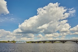 View from the right bank of the Dnieper river over the first metro bridge in Kyiv city with blue subway train, motorboat under it and hotelship behind. Sunny day with blue sky.