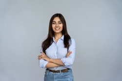 Smiling indian young woman sales professional arms crossed looking at camera isolated on grey blank studio background copy space, happy female student saleswoman girl posing on gray wall, portrait