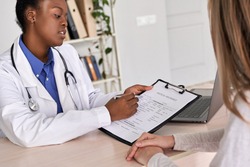 Professional medic female african american doctor showing insurance claim form consult caucasian woman explain information to patient at appointment medical visit in clinic. Medicine women healthcare
