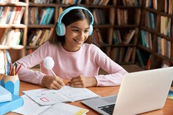 Happy indian latin preteen girl school pupil wearing headphones distance learning online at virtual class with teacher tutor on laptop by video conference call, watching tv lesson at home.