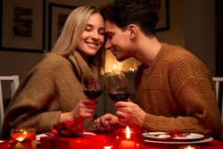 Happy young couple in love clinking glasses drinking wine having romantic dinner date celebrating Valentines Day evening anniversary sitting at table at home or in restaurant. Valentine's Day concept