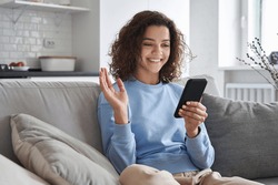 Happy hispanic teen girl waving hand using smartphone app enjoying online virtual chat video call with friends in distance mobile chat virtual meeting, recording stories for social media at home.
