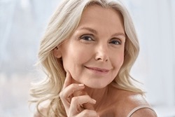 Smiling happy attractive 50s middle aged mature blond woman, old lady looking at camera advertising anti age face skin and body care treatment cosmetics posing in bathroom. Close up headshot portrait