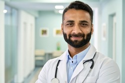 Smiling bearded male Indian doctor wearing medical coat looking at camera. Headshot portrait of ethnic hispanic man medic professional, hospital physician, confident practitioner or surgeon at work.