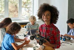 Happy African American junior school kid holding robotic car looking at camera at STEM class. Smiling black child preteen girl posing with robot vehicle. Portrait. Engineering and coding education.