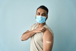 Happy healthy young Indian man wearing face mask showing bandage plaster on arm shoulder after getting vaccination. Vaccine and people inoculation, immunity for covid prevention concept. Portrait