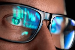 Focused crypto trader analyst wearing eyeglasses working looking at computer screen reflecting in glasses analyzing online trading stock exchange market data charts. Close up eye reflection.