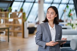 Young Asian business woman entrepreneur standing in office holding digital tablet. Businesswoman leader, professional company manager using smart corporate management technology looking at copy