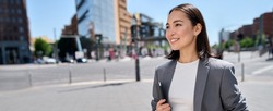 Young smiling proud successful Asian business woman, professional entrepreneur, office employee wears suit standing on city street looking in future career, thinking of success and leadership