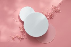 White round podium pedestal cosmetic beauty product presentation empty mockup on trendy pink coral pastel background with light shadows and spring flowers, minimalist flat lay backdrop, top view.