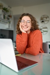 Young happy pretty business woman student sitting at desk at home office with laptop computer looking at camera advertising online learning, remote work, business webinars. Vertical portrait.
