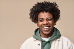 Happy young African American gen z guy winking isolated on beige background. Playful ethnic teen student, cool curly generation z teenager smiling with white perfect teeth, close up portrait.