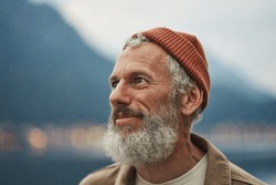 Happy older bearded man standing in nature park enjoying landscape. Smiling active mature traveler looking away exploring camping tourism nature mountains view feeling freedom. Close up portrait