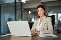 Happy mature business woman entrepreneur in office using laptop at work, smiling professional middle aged 40 years old female company executive wearing suit working on computer at workplace.