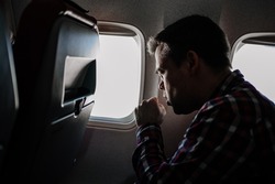 a man in a plaid shirt coughs on the plane in a window seat. flying in an airplane during illness. without the use of personal protective equipment in public places.