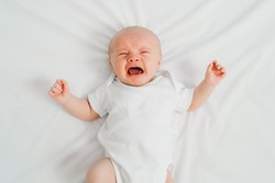 a newborn baby cries on a white sheet. childish tantrums. colic and abdominal pain in infants. medicines and vitamins for babies. top view.