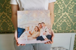 woman holds book with photos of big family at home. Photobook is gift. professional photographer and designer. printing of photos and journals in photo laboratory.