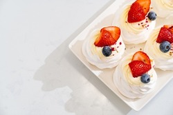 strawberries, blueberries and cream decorates to Anna Pavlova cakes on a white plate. recipes for delicious traditional desserts. cooking school and courses. confectionery cafe menu