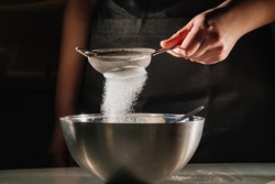powdered sugar or flour is sifted into a bowl on a black background. recipes for pastries and desserts. cooking school and master classes for cooks and housewives. confectionery. cooking class