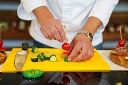 a male cook makes canapes and strings a tomato and cucumber on skewers. sandwiches with pate and vegetables. master class on the preparation of snacks.
