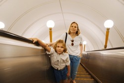 Mom and daughter ride up the escalator in the subway. Long journeys and the road in a big city.