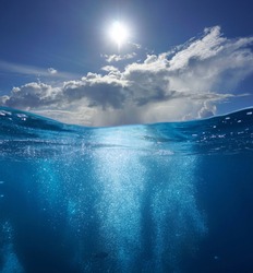 Seascape, air bubbles underwater sea and sunny blue sky with cloud, split view over and under water surface