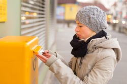 Young woman posting a letter, dropping an envelope in a postbox.