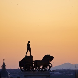 Ancient statue of a roman soldier standing on the coach on the roof of one of the buildings seen from C?rculo de Bellas Artes in Madrid, Spain.